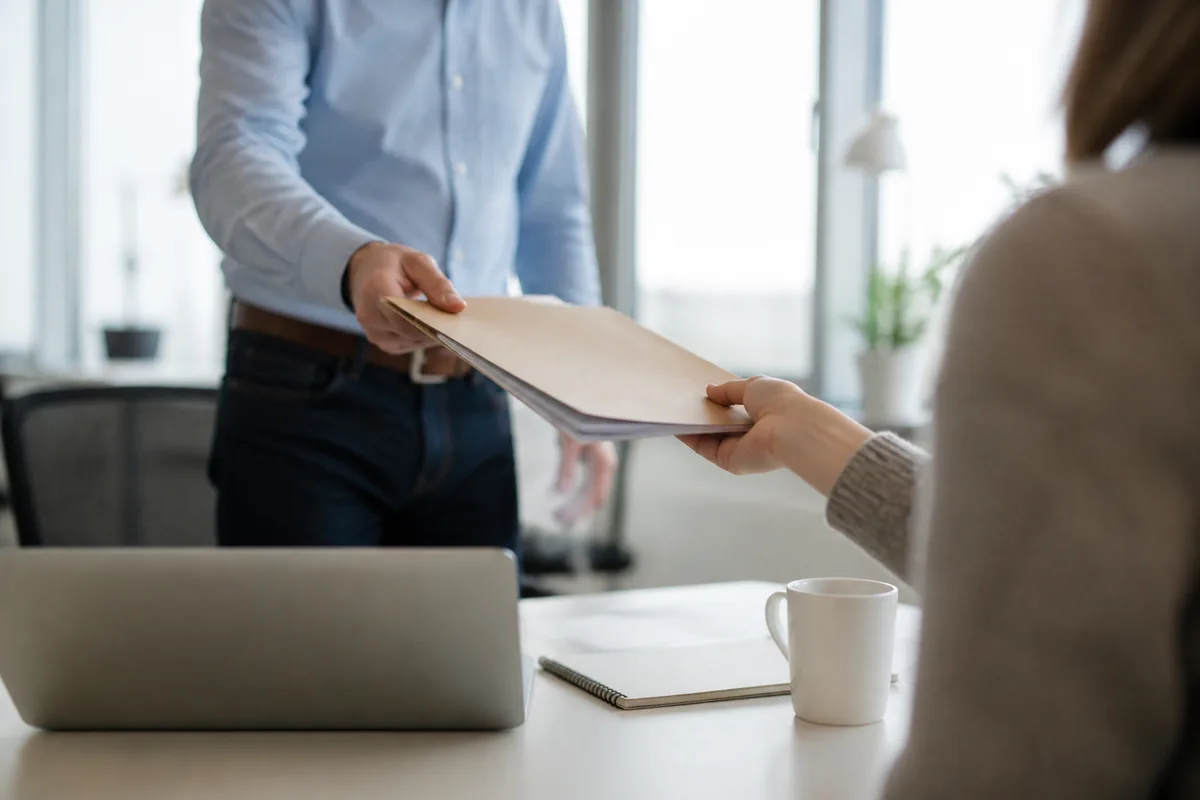Manager transmettant un dossier à un collaborateur dans un bureau lumineux