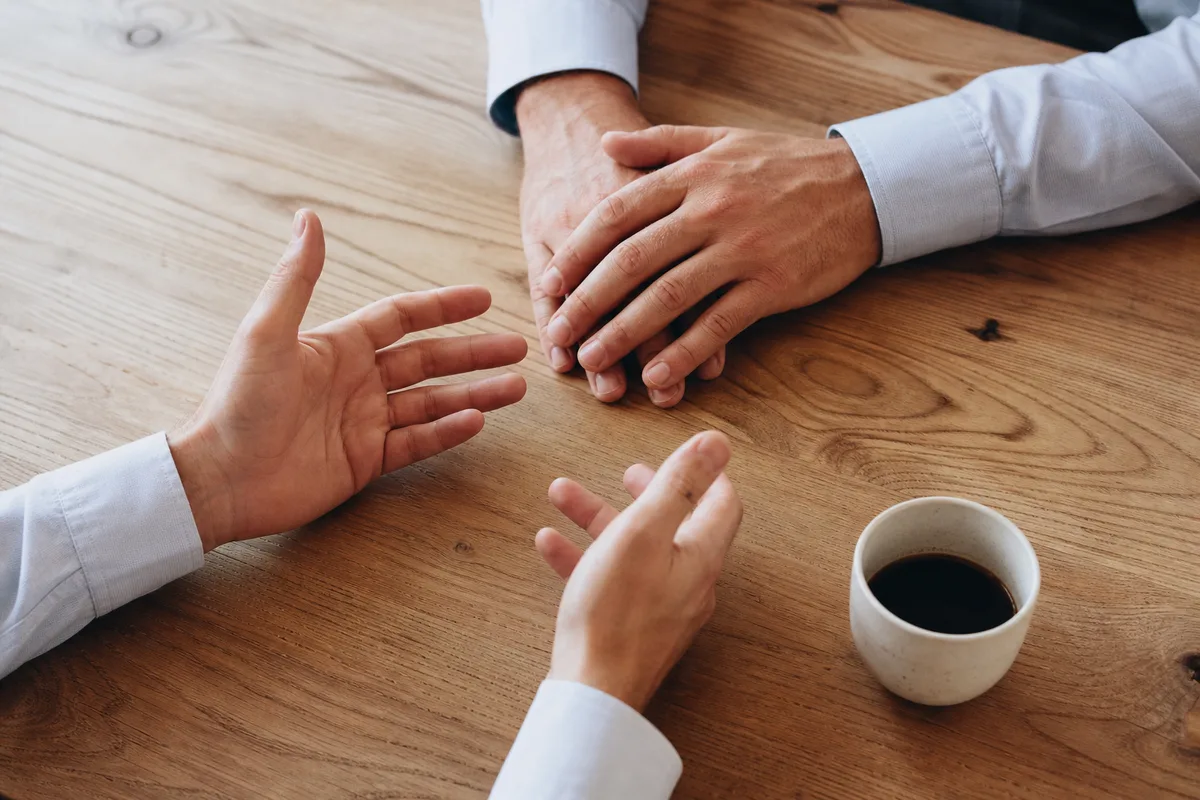 Deux paires de mains posées sur une table en bois clair pendant un échange professionnel
